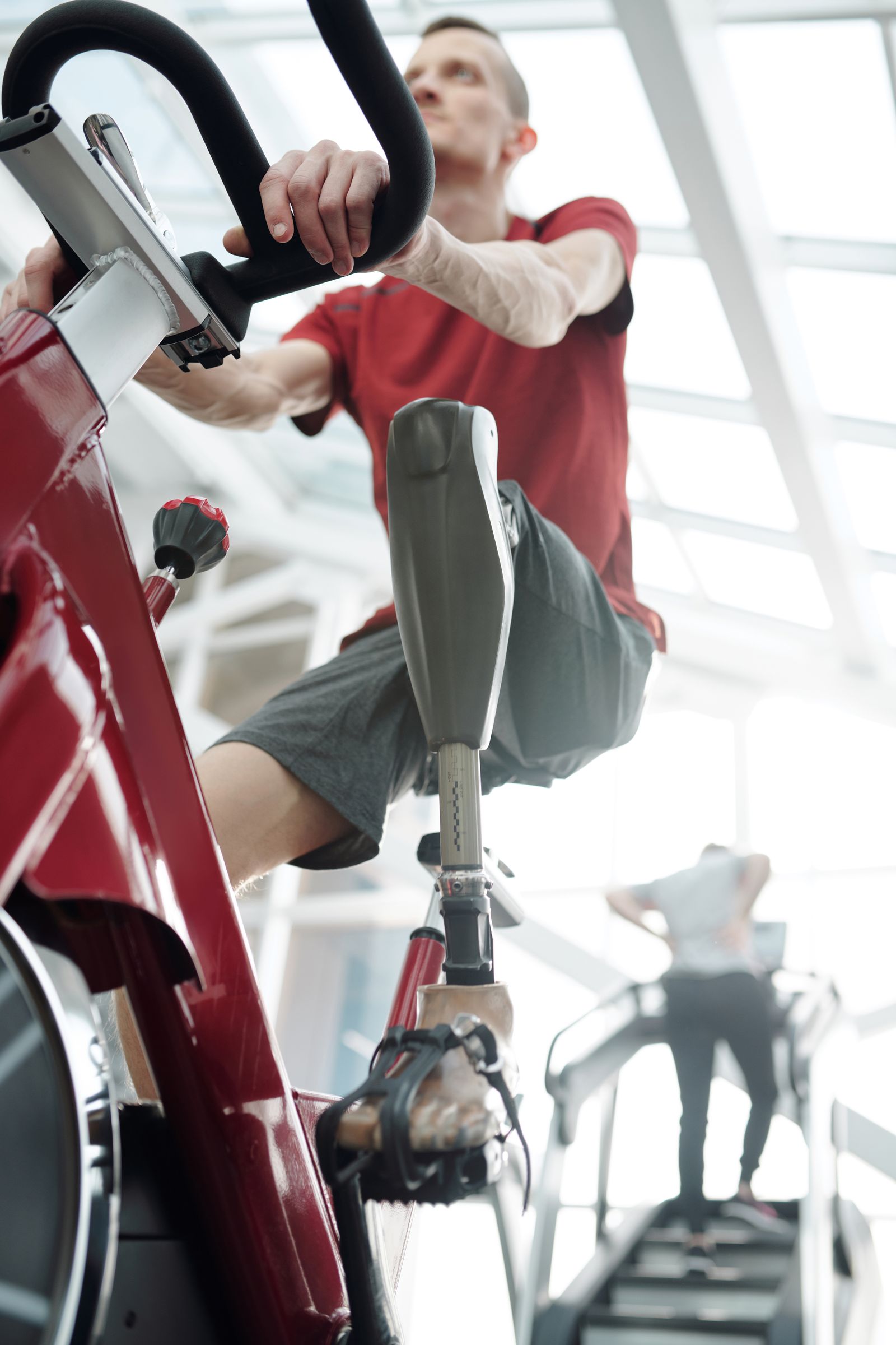 A man in a red t-shirt using a gym exercise bike in everyday training clothes