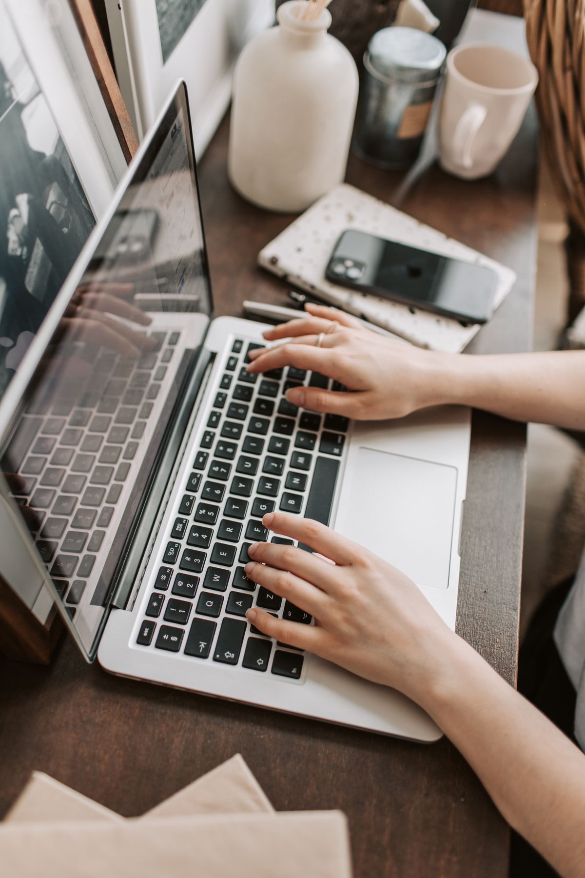 Hands typing on a laptop beside a face-down phone on a wooden desk
