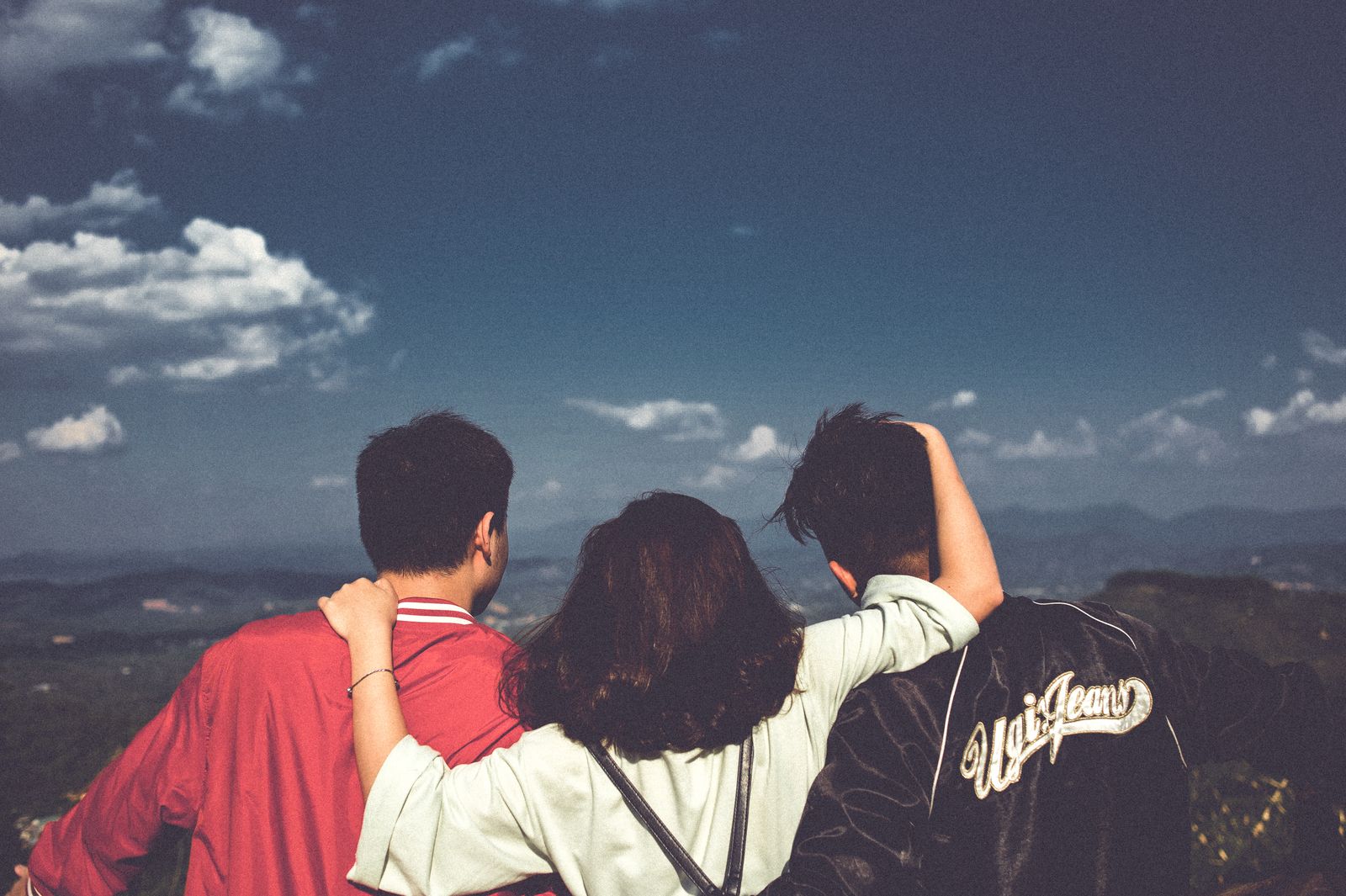 Three friends in jackets standing together looking out over hills
