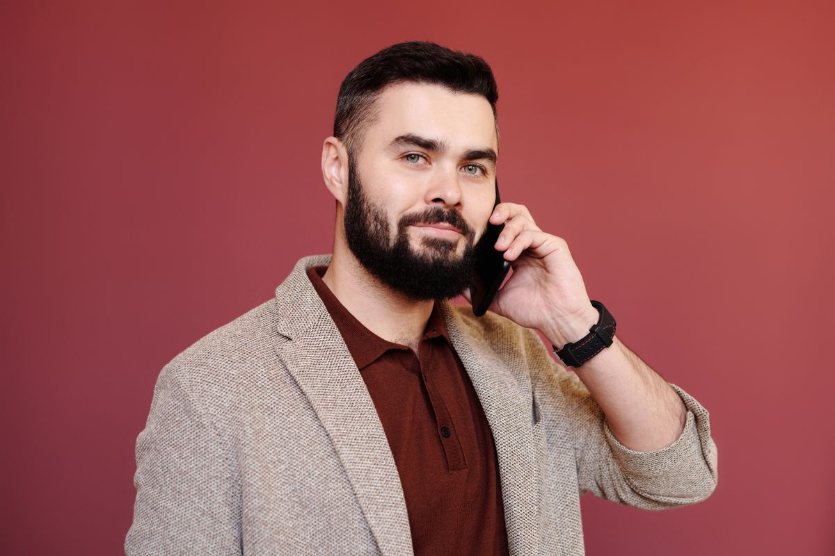 A bearded man in a beige blazer and polo shirt talking on a mobile phone