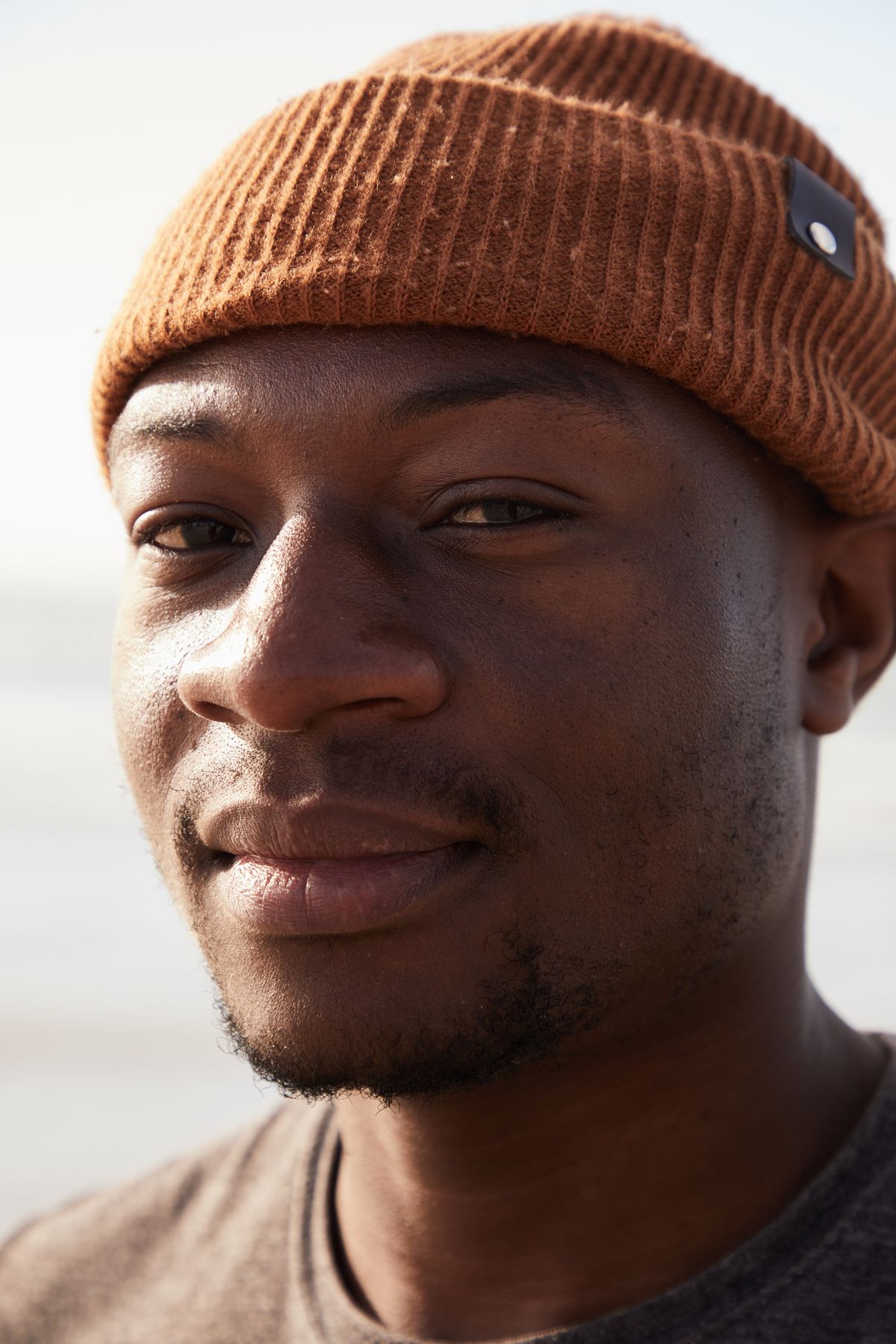 A man in a brown beanie standing outdoors in natural daylight