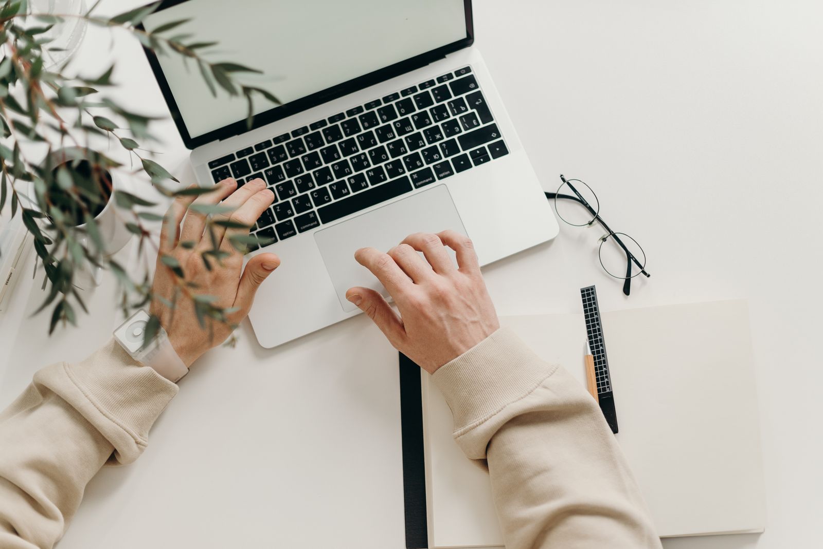 Person in a beige jumper typing at a laptop on a pale desk