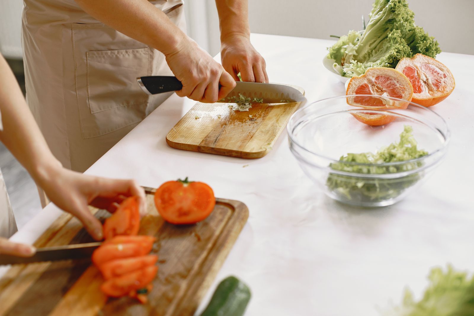 Two people in aprons chopping tomatoes and salad vegetables on a kitchen counter