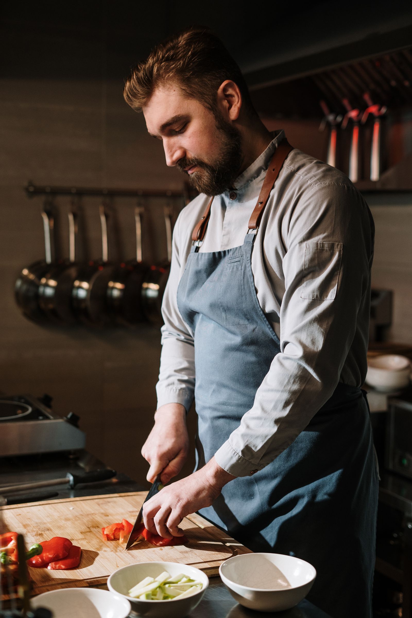 A cook in a long-sleeve shirt chopping red peppers on a wooden board