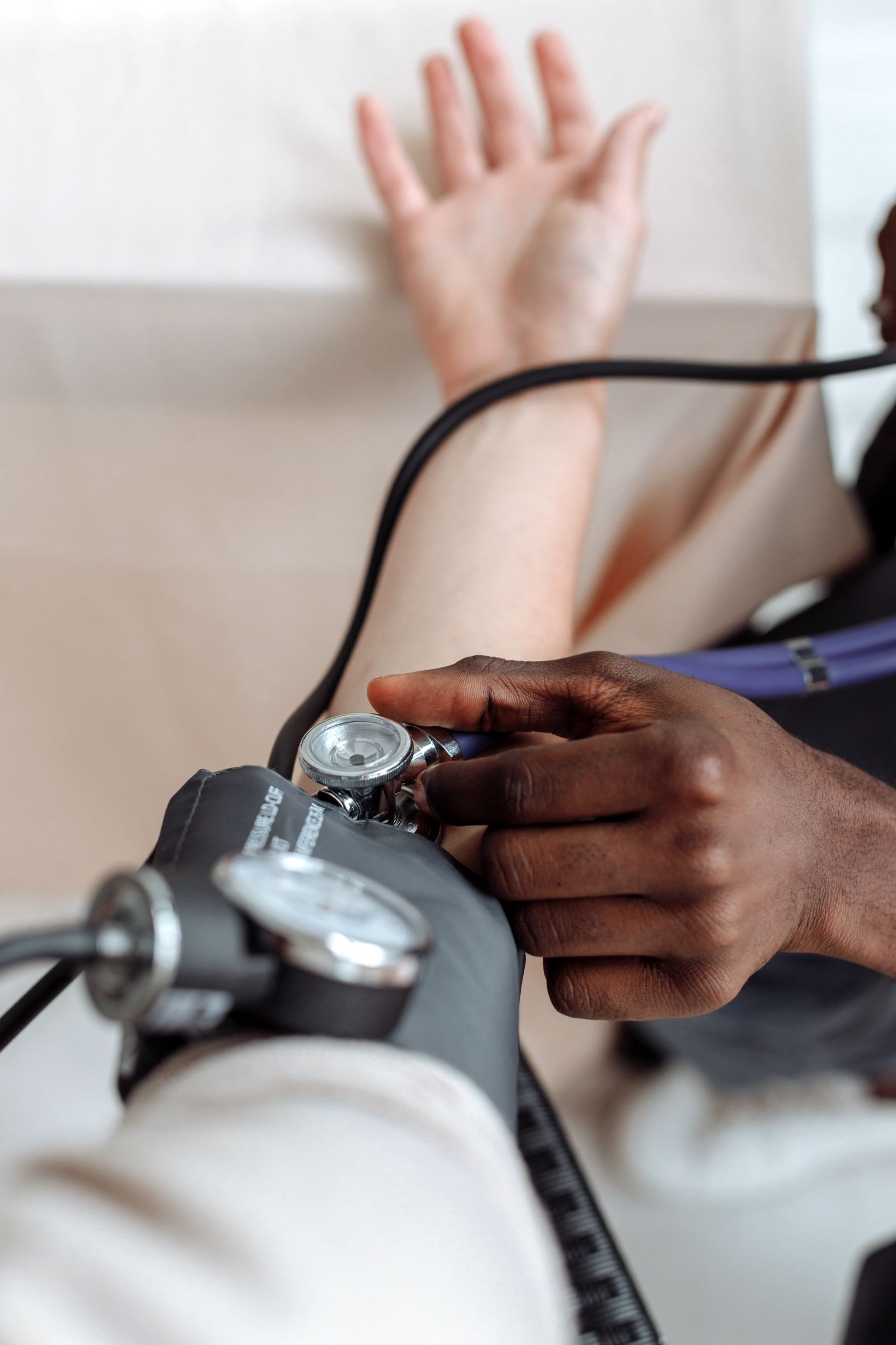 A clinician in work clothes checking a seated patient's blood pressure in clinic