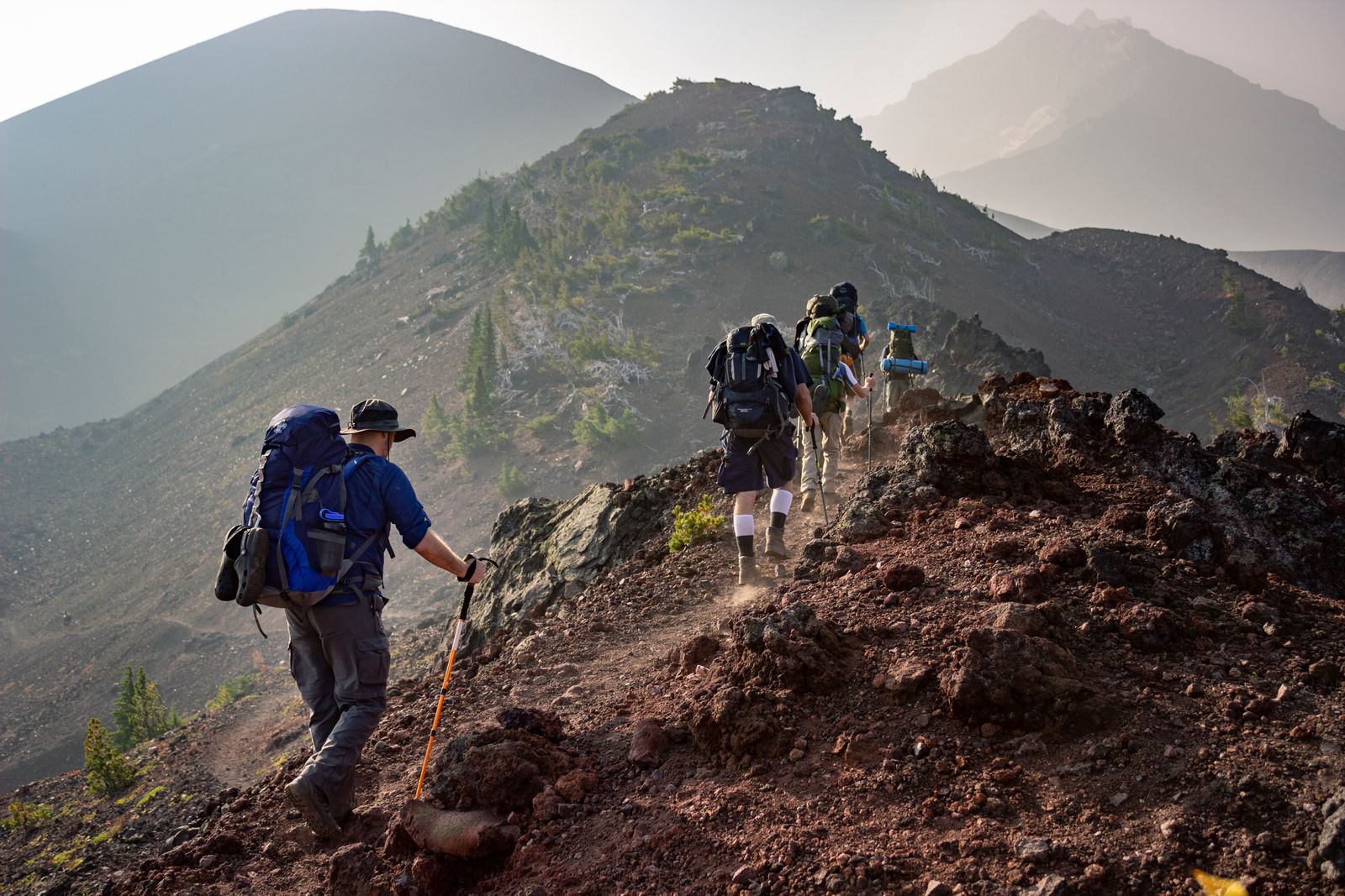 A group of hikers in jackets and trousers walking a mountain ridge with backpacks