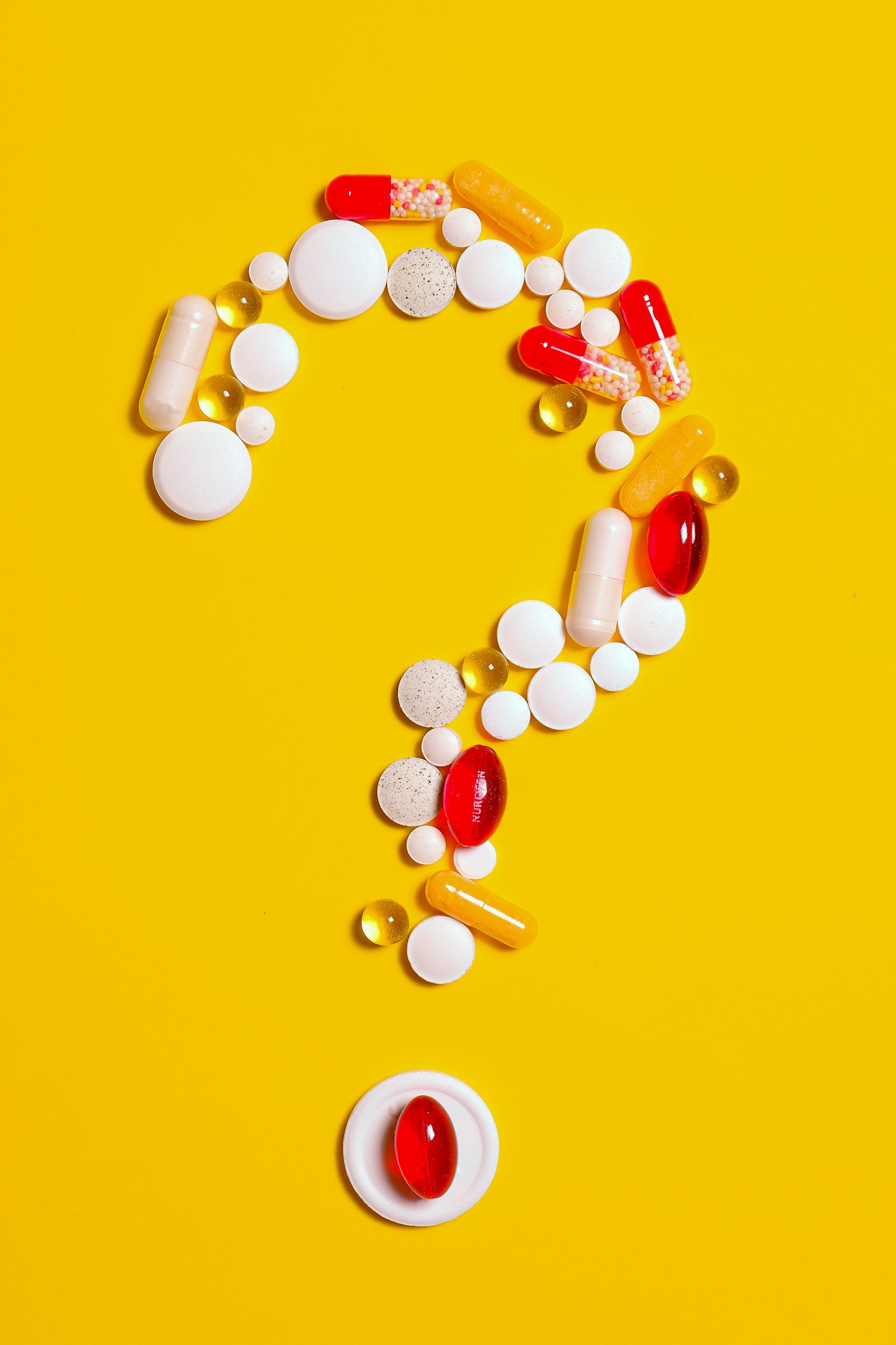 Red, white and yellow capsules arranged as a question mark on a yellow background