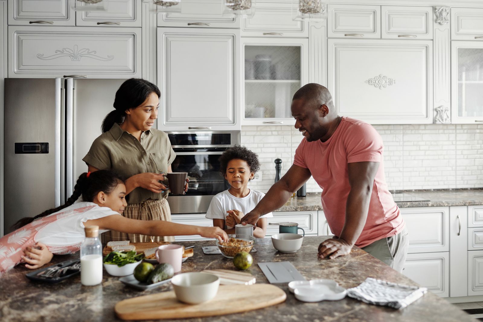 A man in a pink t-shirt preparing breakfast with family at a kitchen island