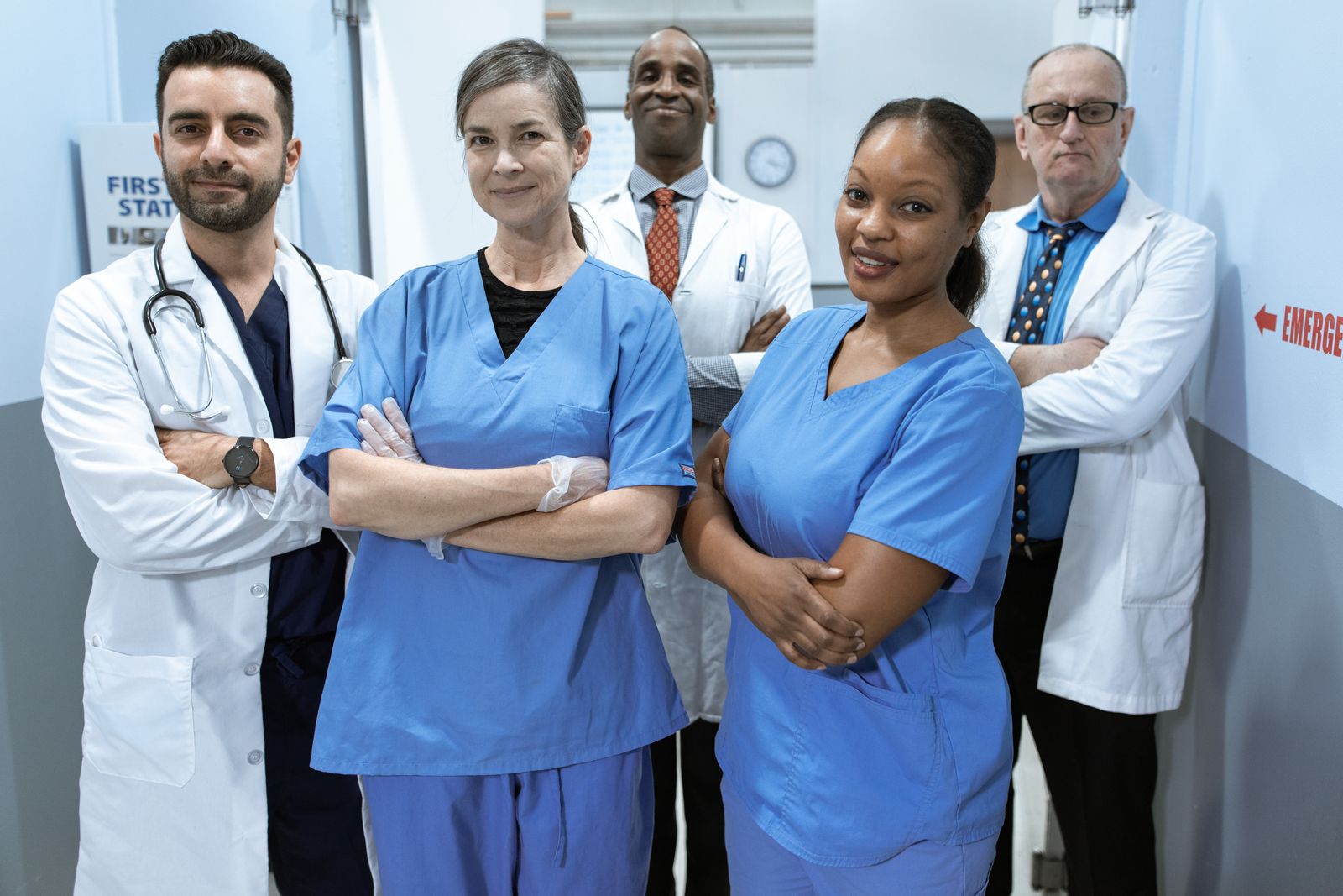 A mixed clinical team in white coats and blue scrubs standing together in a hospital corridor