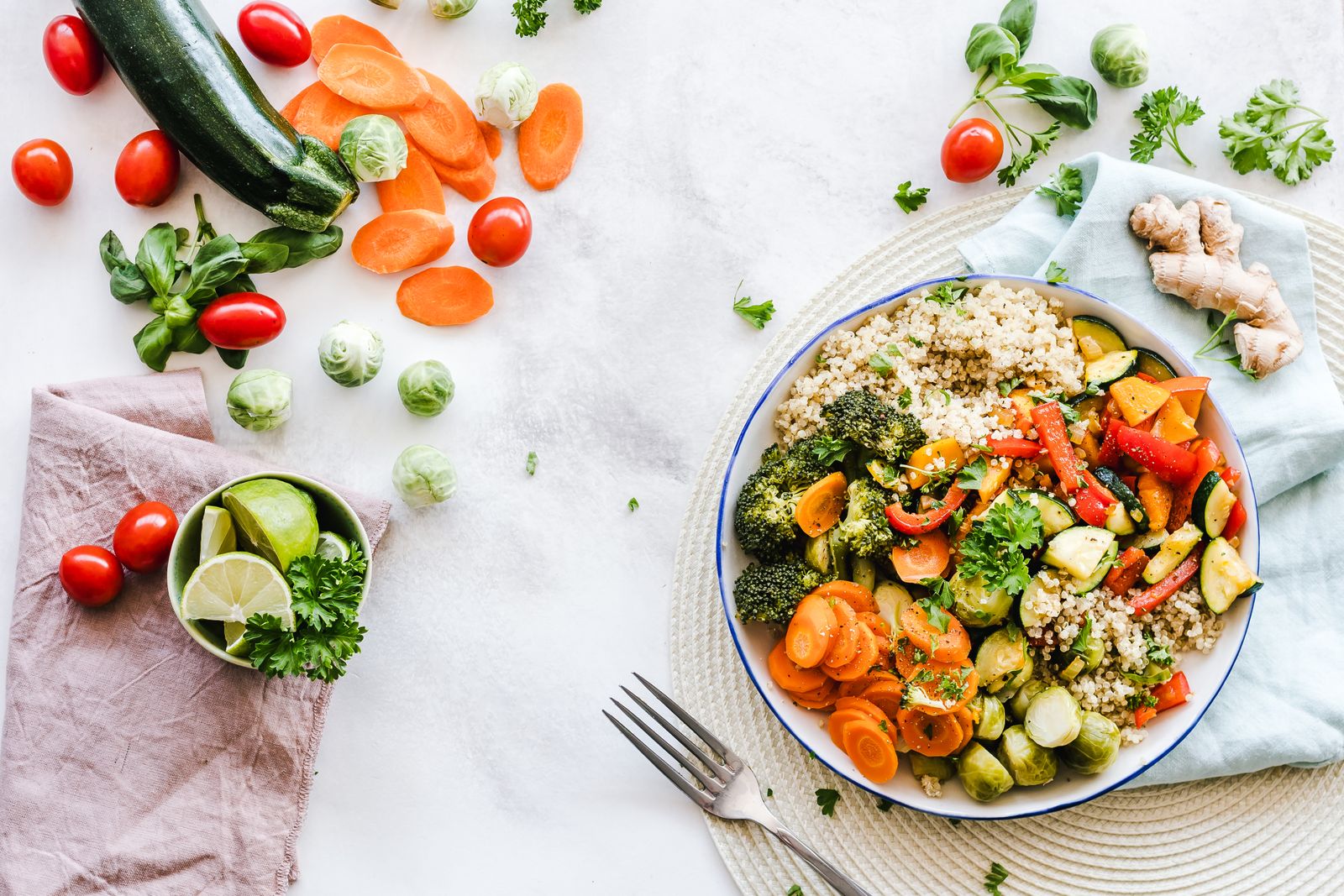 A bowl of quinoa with roasted carrots, broccoli, peppers and Brussels sprouts on a white table