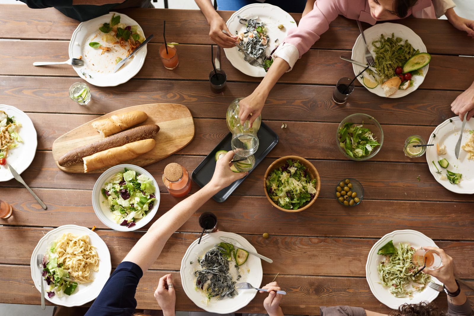 An overhead view of a shared dining table with leftover pasta, salad bowls, and bread after a meal