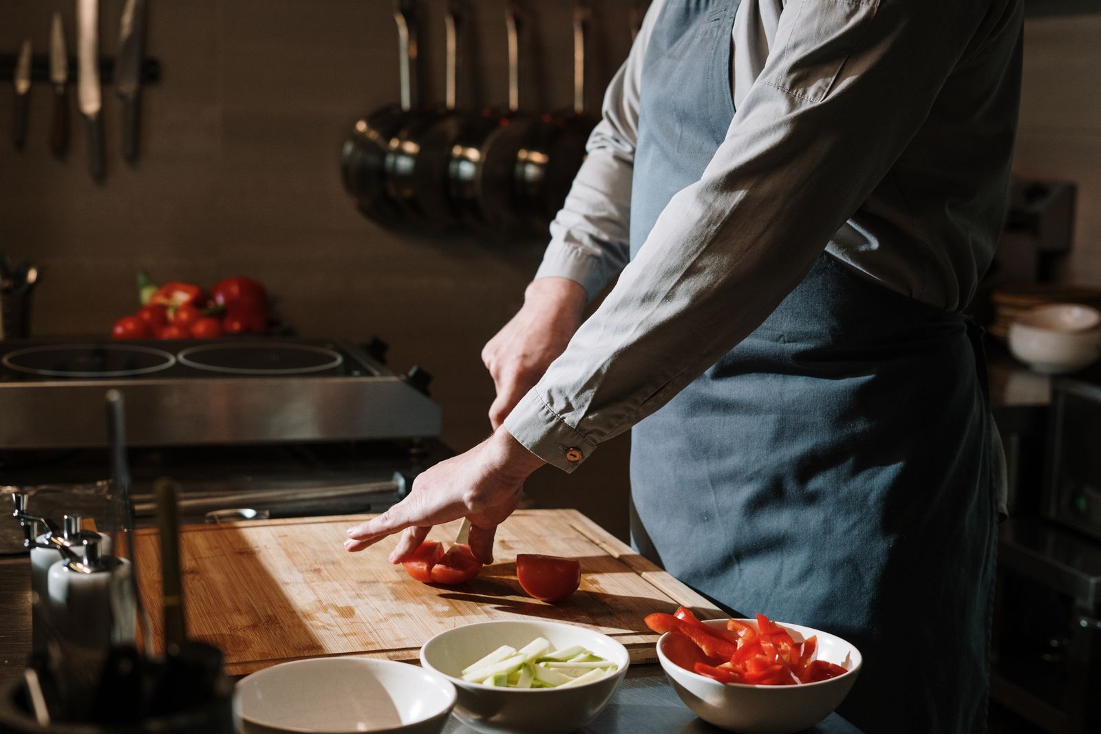 A cook in a long-sleeved shirt and apron slicing tomatoes on a wooden board