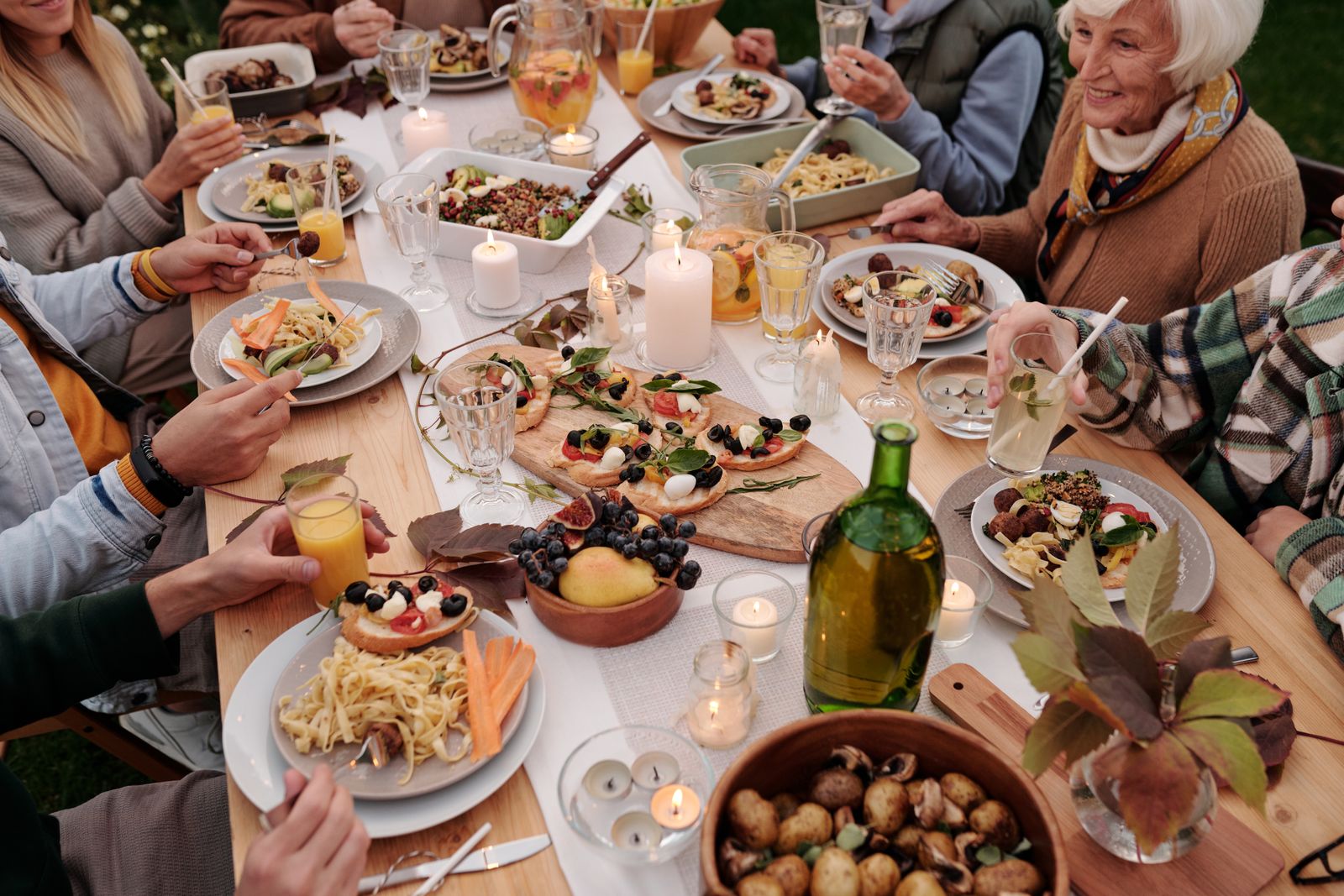 Older and younger relatives in jumpers sharing an outdoor meal of pasta, bread and fruit