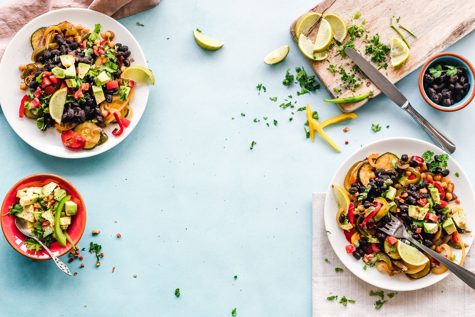 Two plates of mixed vegetables, beans and lime on a pale blue table
