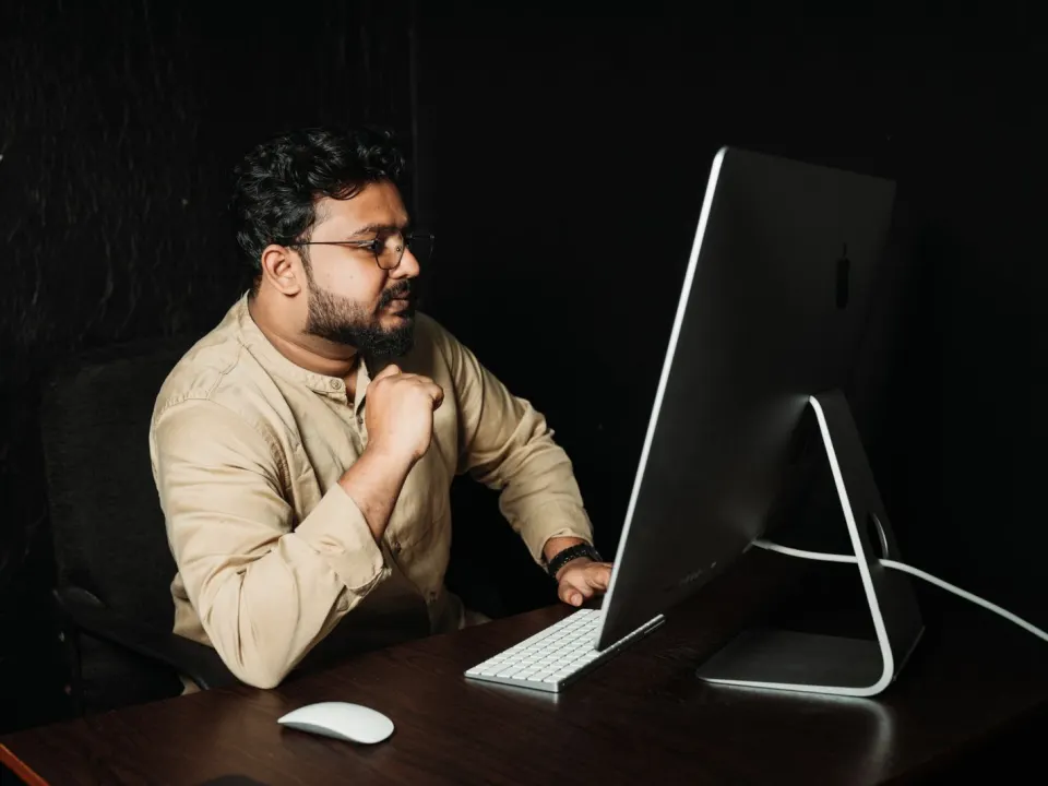 Man in a jacket using a laptop at a wooden table with hands on the keyboard
