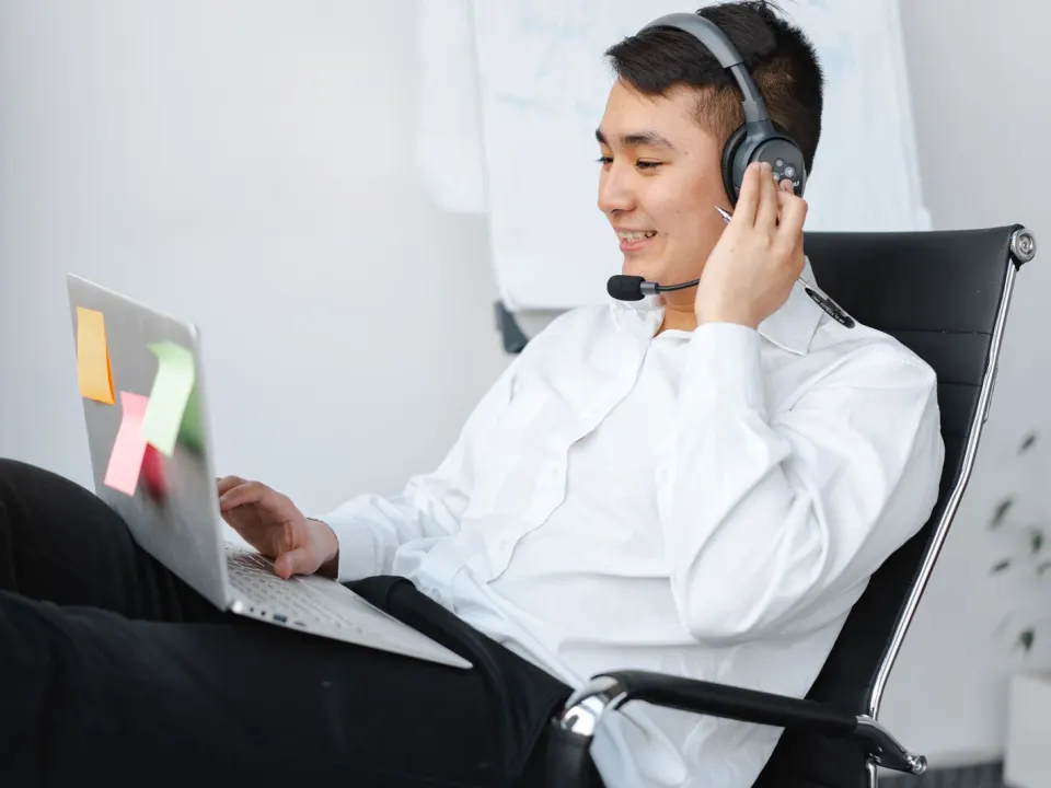 Man in a long-sleeved top working at a laptop with a headset at a desk