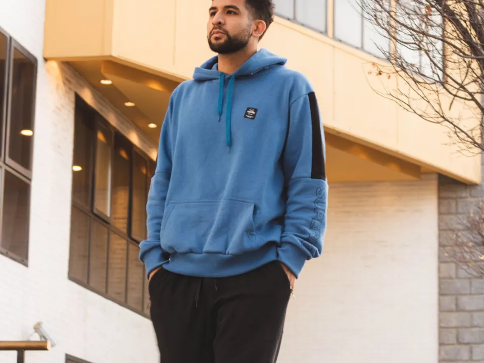 A man in a blue hoodie and dark trousers walking on a city pavement