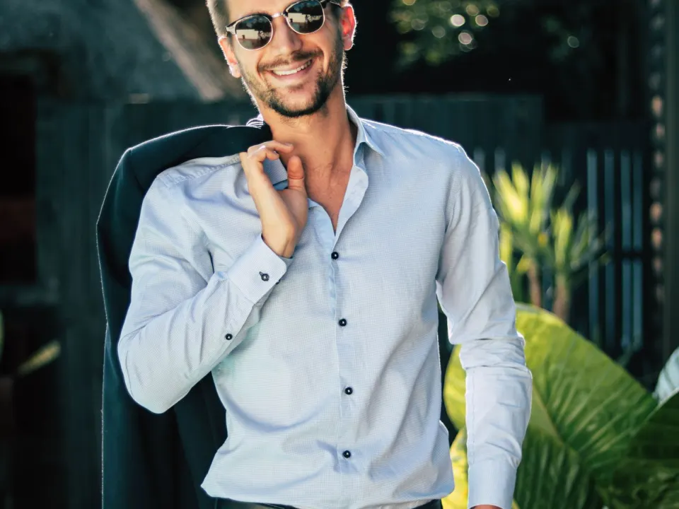 Man in a light shirt and dark trousers standing outdoors in everyday clothes
