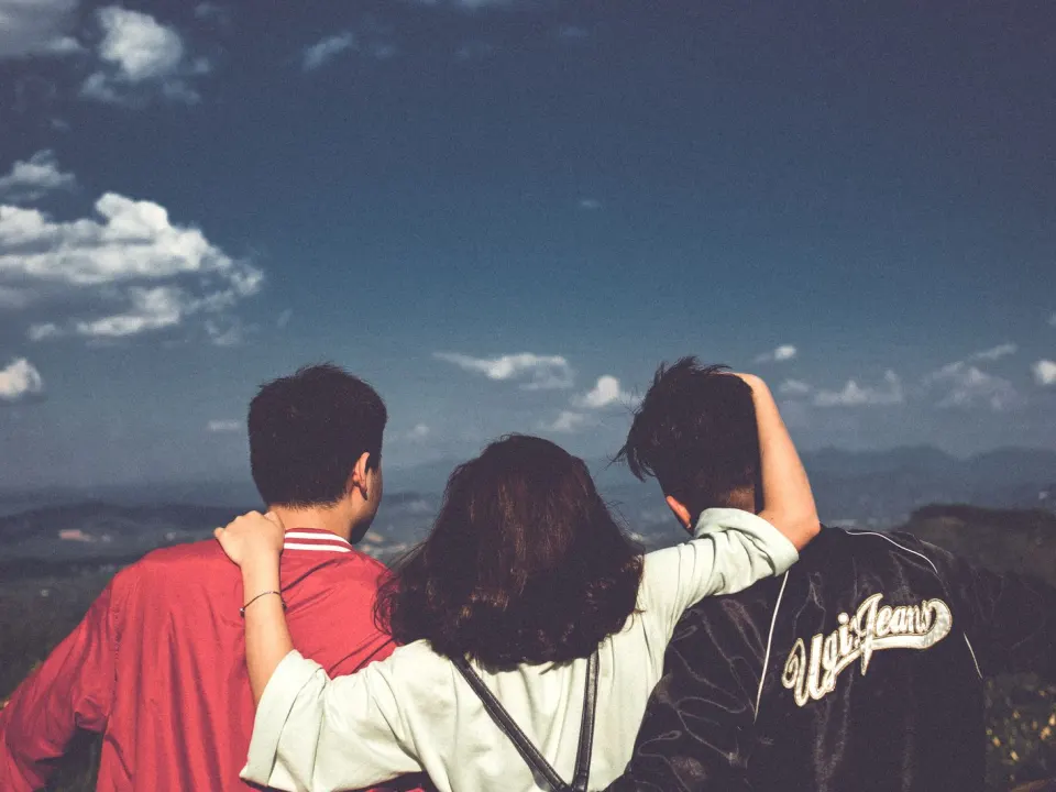 Three friends in jackets standing together looking out over hills