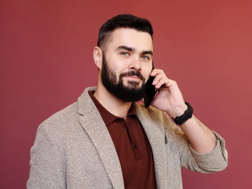 A bearded man in a beige blazer and polo shirt talking on a mobile phone