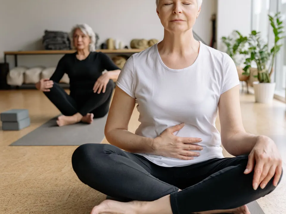 Two women in t-shirts sitting on yoga mats during a small indoor class