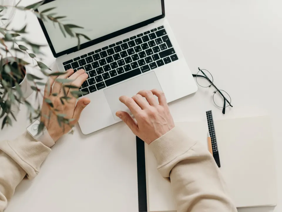 Person in a beige jumper typing at a laptop on a pale desk