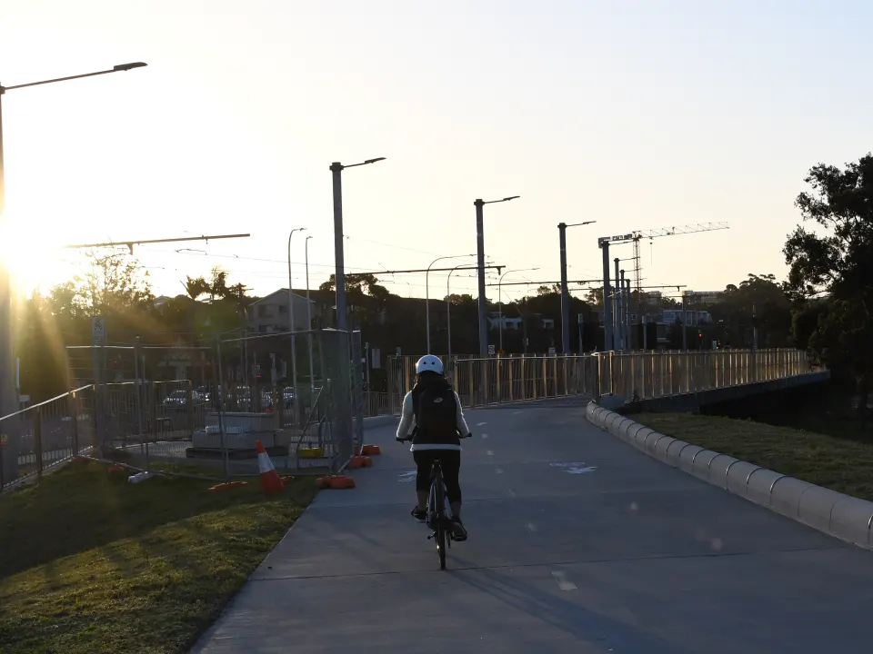 A cyclist in a helmet rides on a suburban paved path beside grass