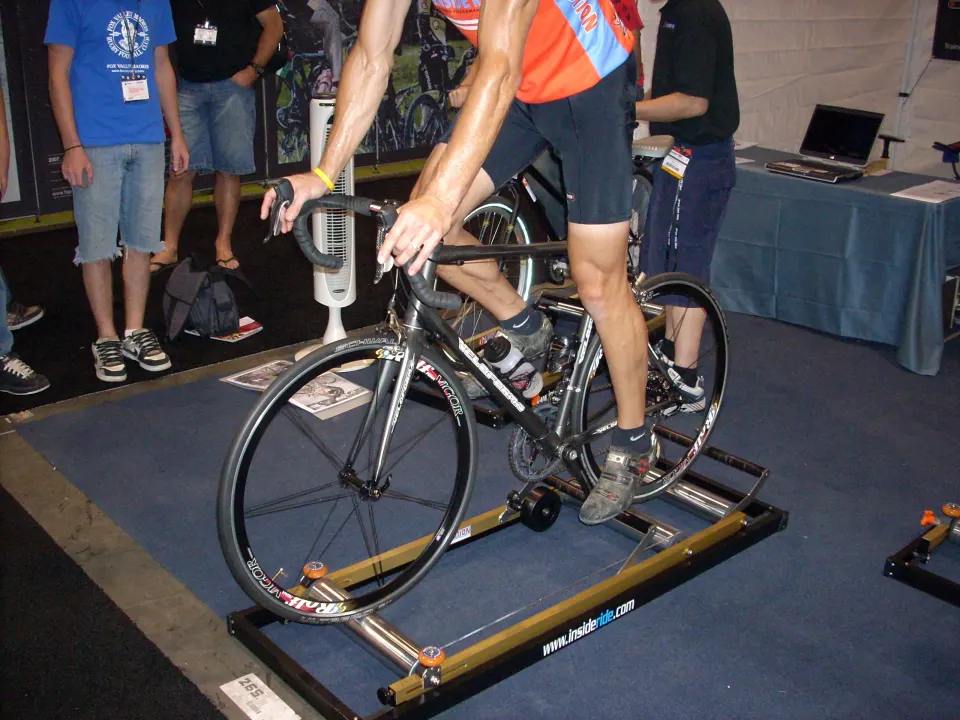 A road bike mounted on a simple indoor trainer in a room
