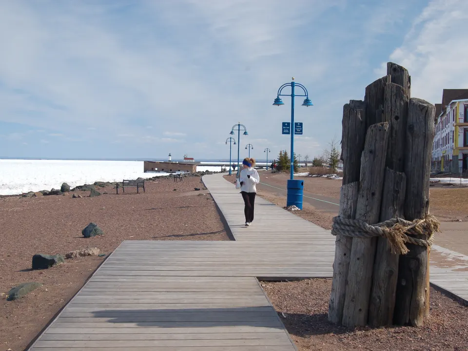 A person in a white jacket on a lakeside boardwalk