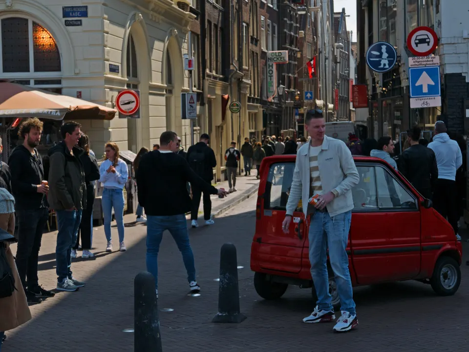 People standing and walking at the entrance to a narrow old-city lane in sunlight