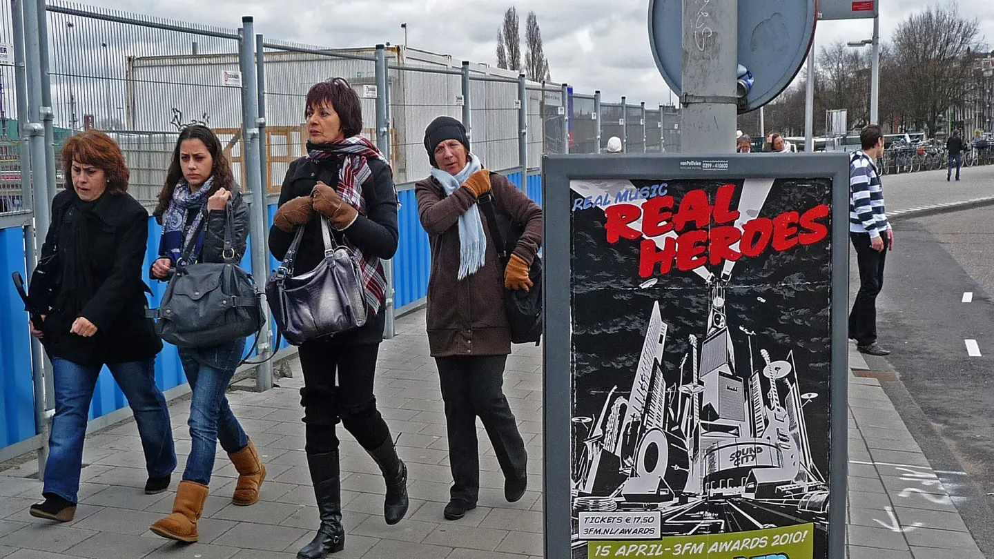 A group of women walking together along a city pavement under a cloudy sky