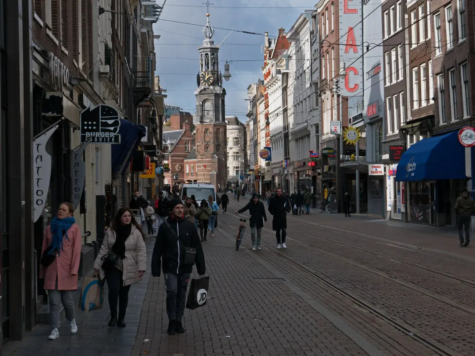 People walking a narrow city street with an old tower in the background