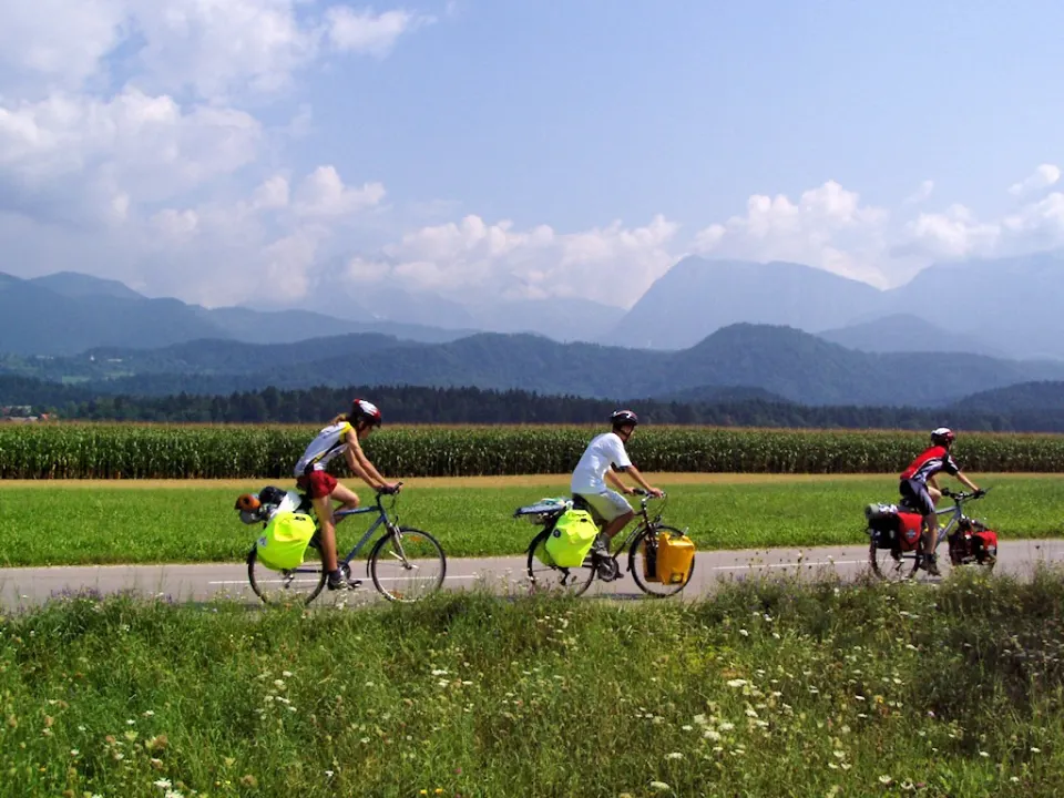 Three touring cyclists on a rural road beside fields in Slovenia