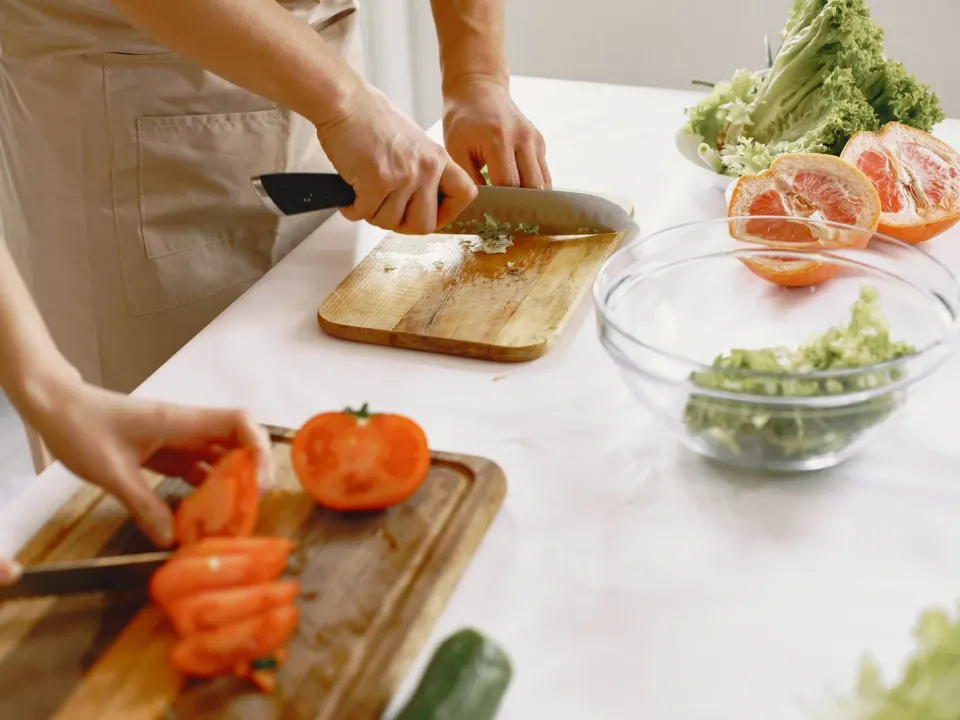 Two people in aprons chopping tomatoes and salad vegetables on a kitchen counter