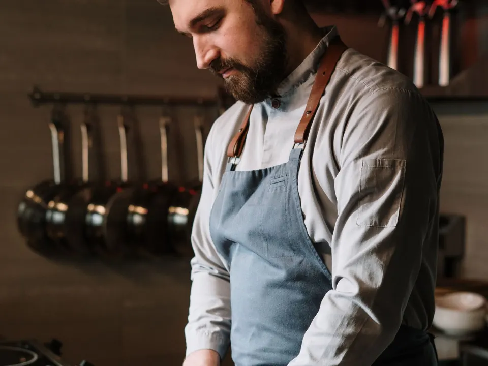 A cook in a long-sleeve shirt chopping red peppers on a wooden board