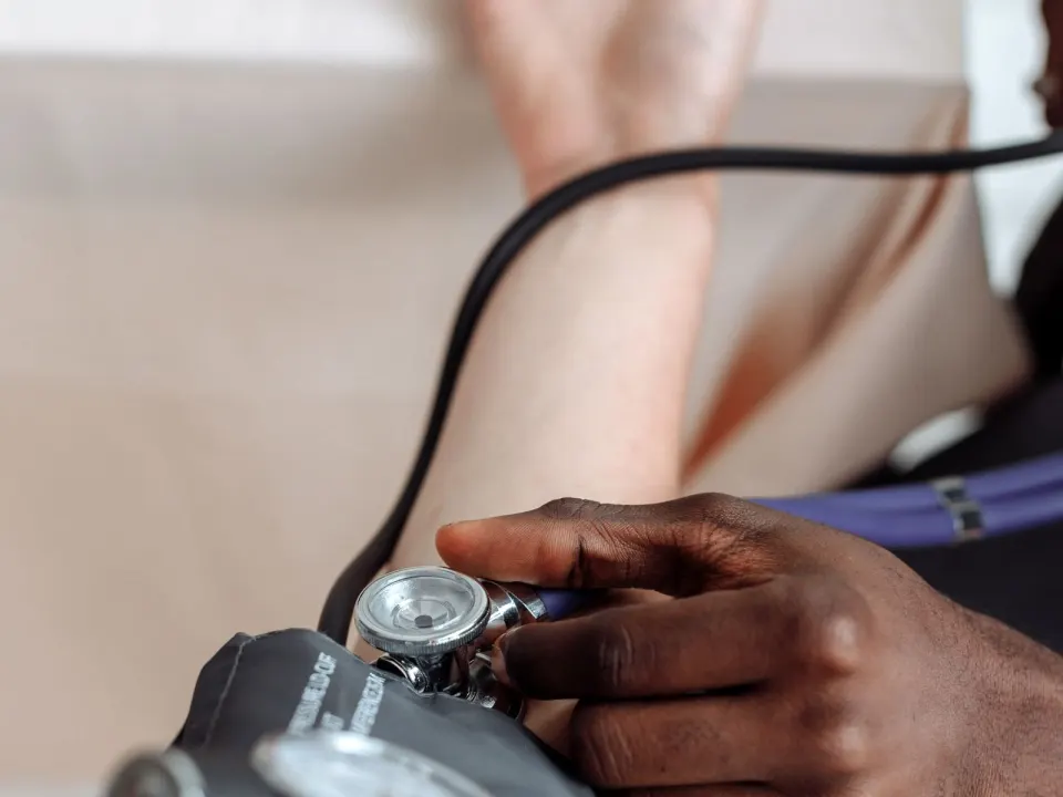 A clinician in work clothes checking a seated patient's blood pressure in clinic