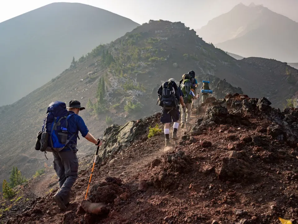 A group of hikers in jackets and trousers walking a mountain ridge with backpacks
