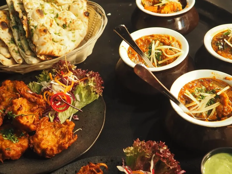 Shared Indian restaurant dishes with naan, curries in bowls, and a side salad on a dark table
