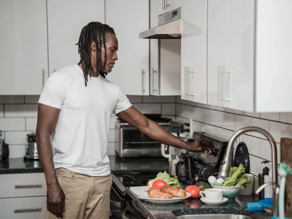 A man in a white shirt cooking breakfast vegetables at a home hob
