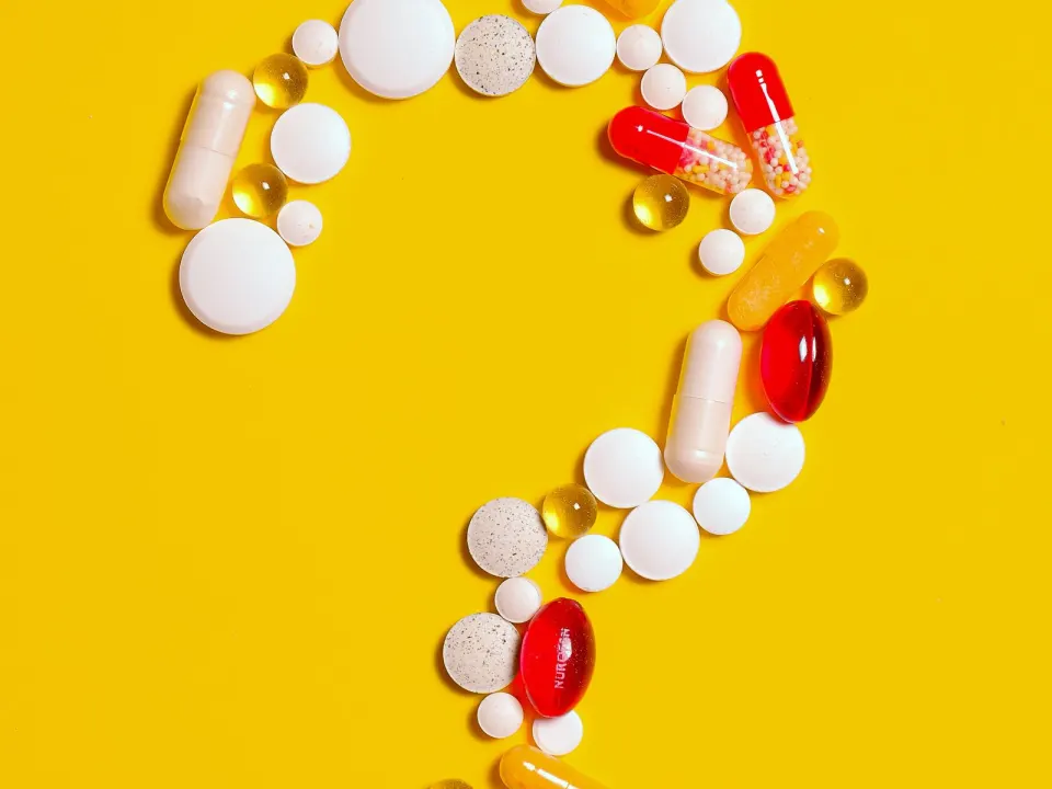 Red, white and yellow capsules arranged as a question mark on a yellow background