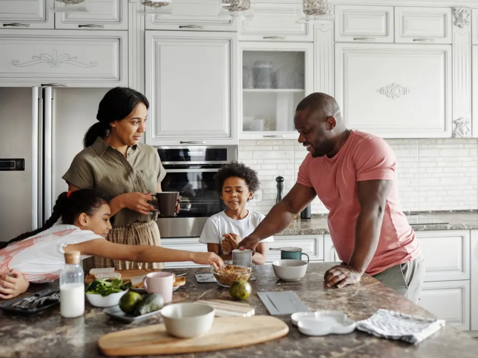 A man in a pink t-shirt preparing breakfast with family at a kitchen island