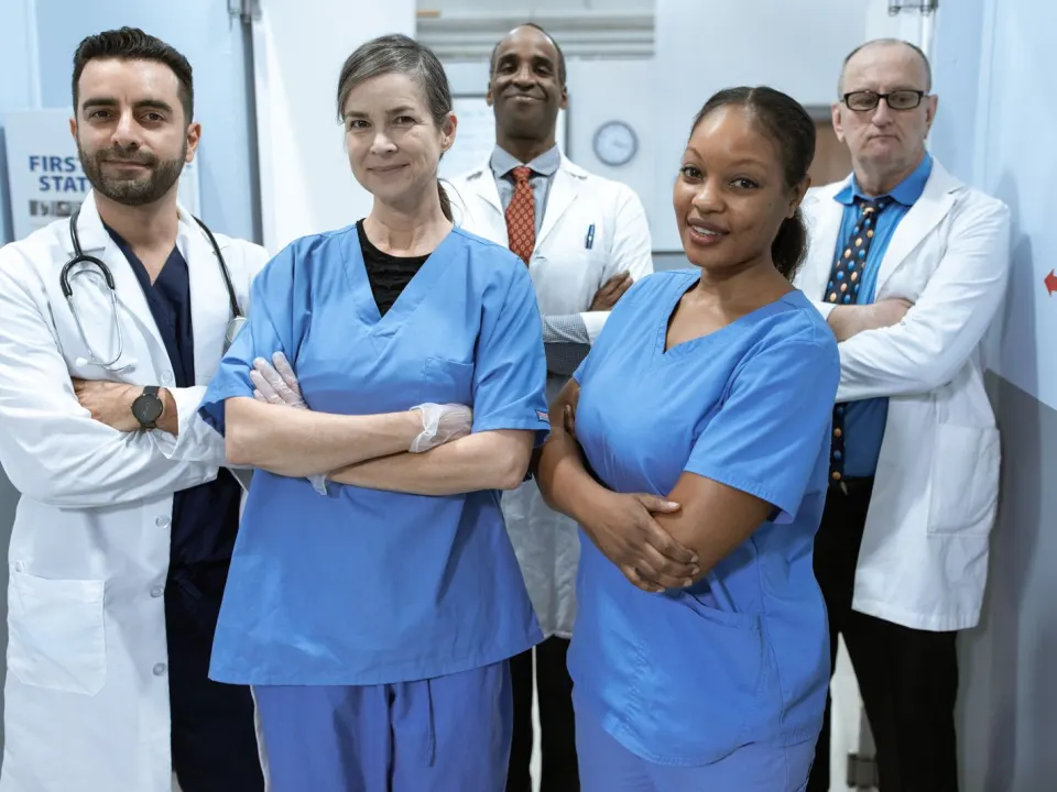 A mixed clinical team in white coats and blue scrubs standing together in a hospital corridor