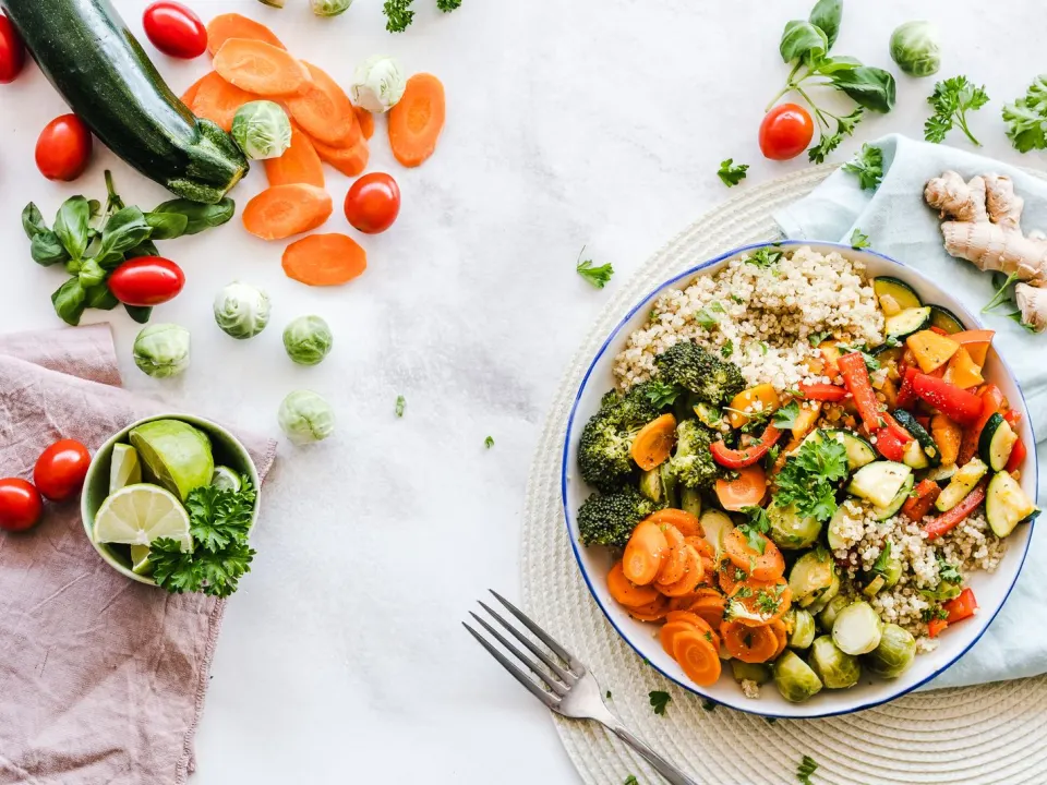 A bowl of quinoa with roasted carrots, broccoli, peppers and Brussels sprouts on a white table
