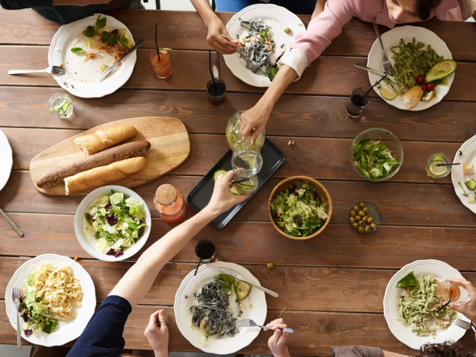 An overhead view of a shared dining table with leftover pasta, salad bowls, and bread after a meal