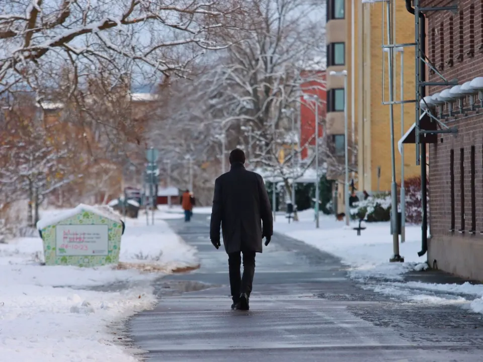 A man in a dark winter coat walking away along a quiet snowy pavement