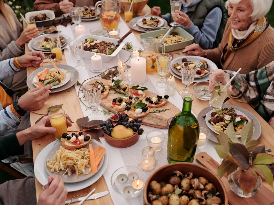 Older and younger relatives in jumpers sharing an outdoor meal of pasta, bread and fruit