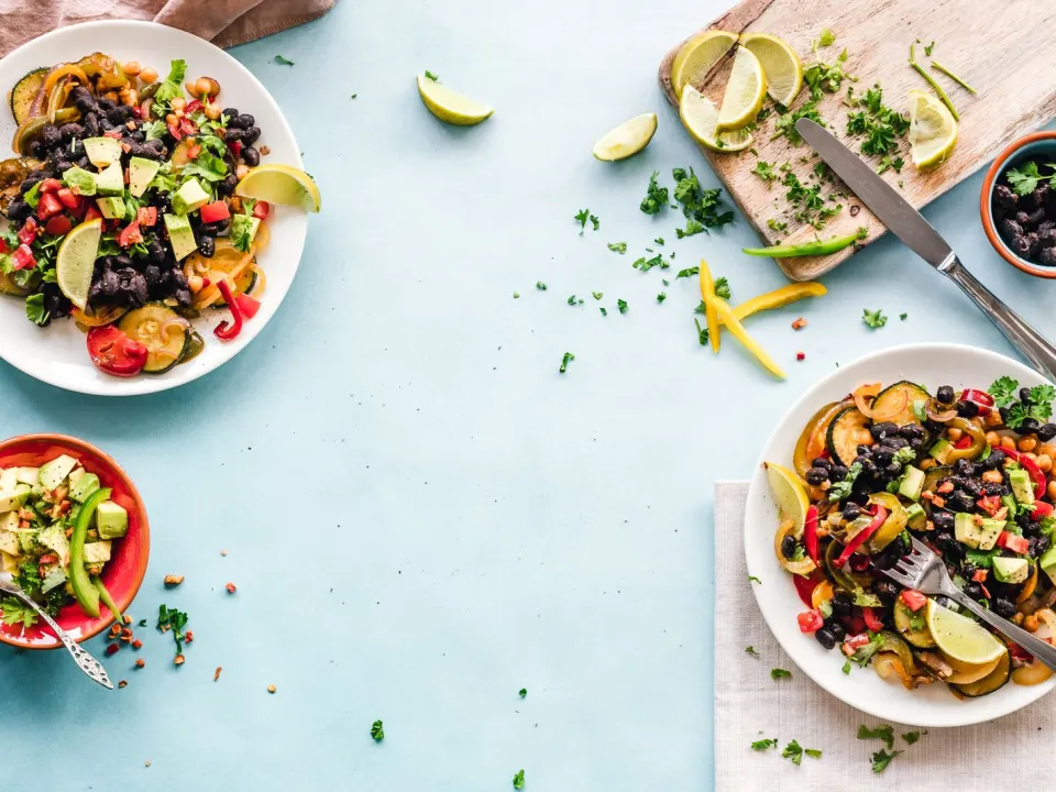 Two plates of mixed vegetables, beans and lime on a pale blue table
